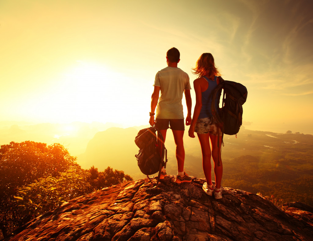 man and woman wearing backpacks at the top of a mountain looking at sunset