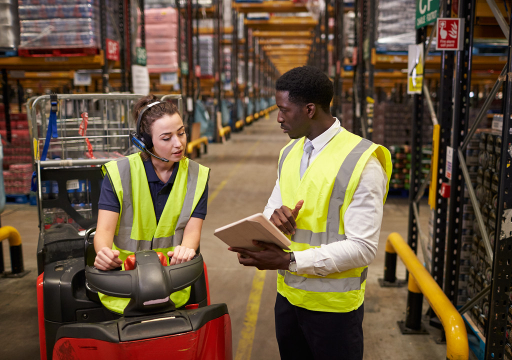 woman in mini vehicle talking to male employee about inventory in the warehouse