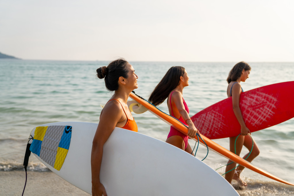 Young women holding surf boards while walking along a beach.