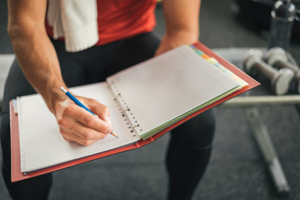 man writing his fitness routine in a notebook at the gym